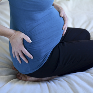 Pregnant mother sitting on bed holding stomach
