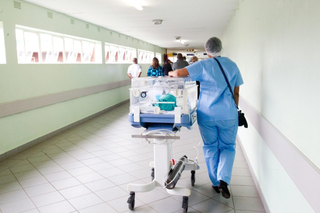 Image of a hospital hallway with a nurse pushing a pediatric hospital bed. Even in moments like this, systemic negligence can cause issues that increase the likelihood of patient injury.