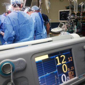Hospitals build causation defense narratives around inevitability of injury. Photo shows doctors and surgeons around an operating table with a heart monitor in the foreground.