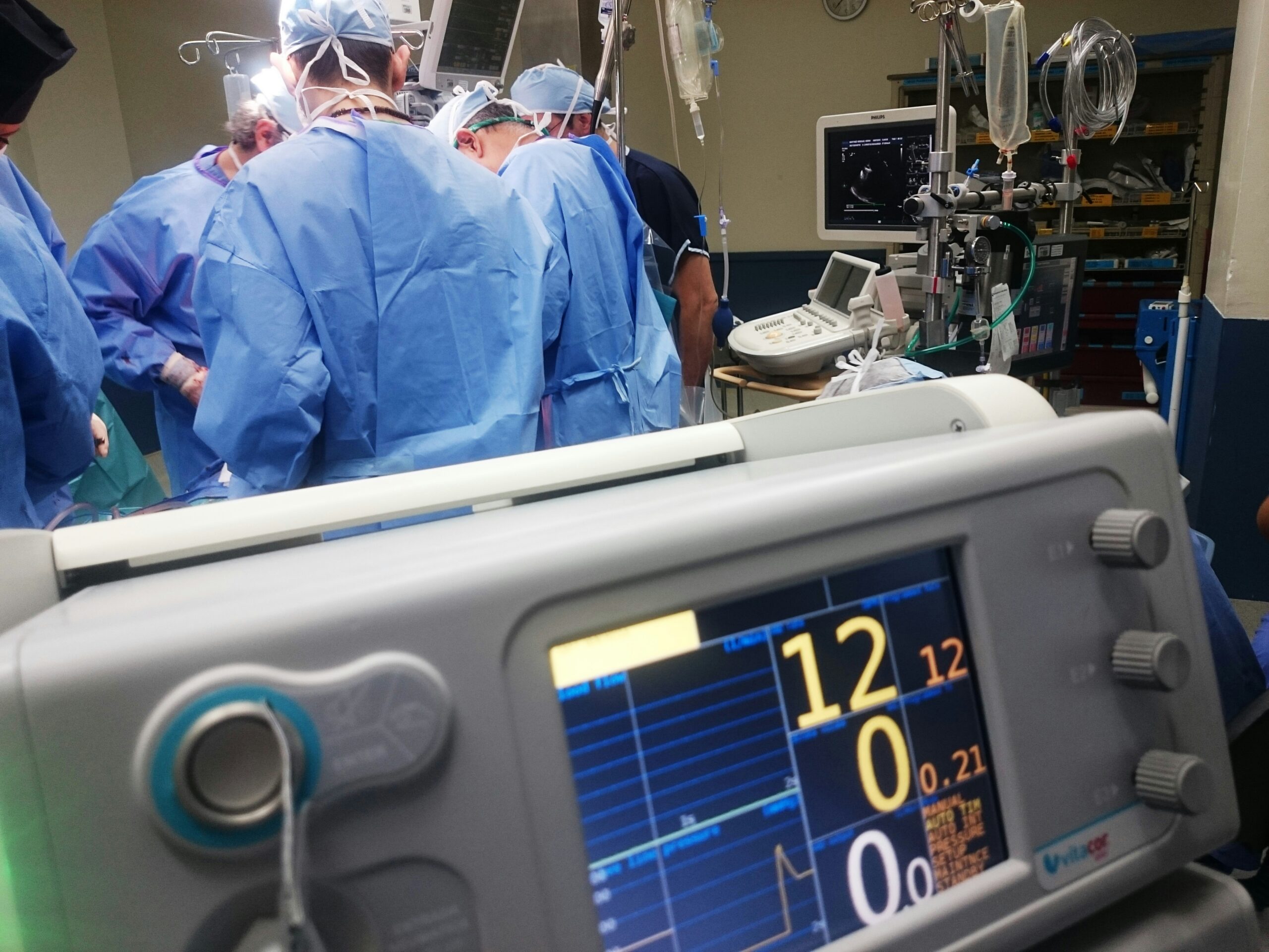 Hospitals build causation defense narratives around inevitability of injury. Photo shows doctors and surgeons around an operating table with a heart monitor in the foreground.