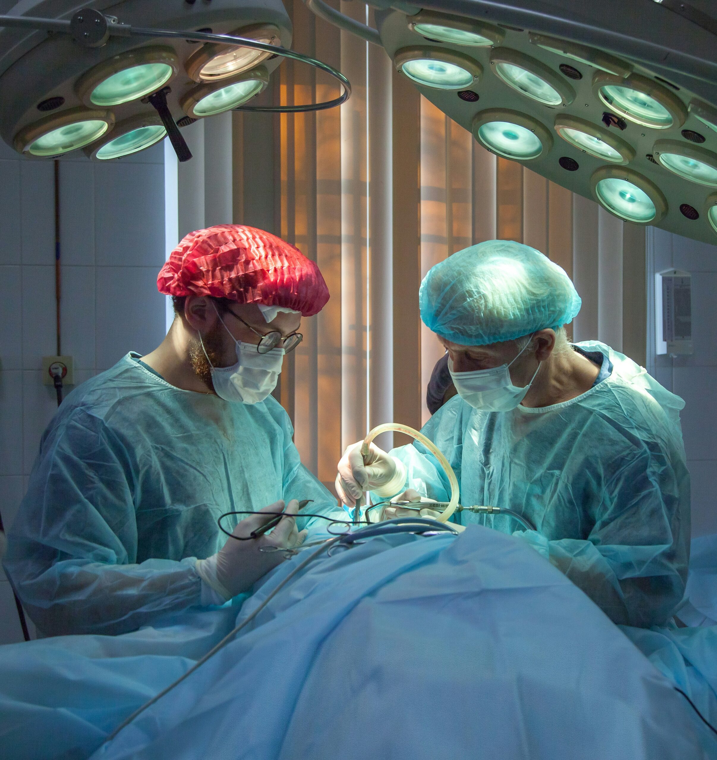 Two surgeons working on a patient, one in a red cap, the other in blue. This is symbolic of competing medical testimony, where two experts go head to head to try and explain how an injury occurred.