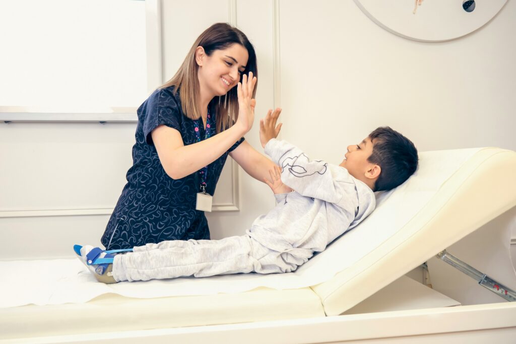 A nurse giving a child laying in a hospital bed a high five. Despite pediatric stroke, the child is recovering.