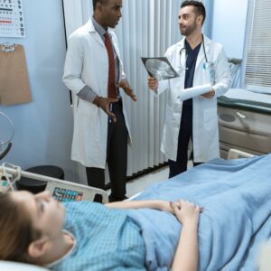 Two doctors discussing an image of a brain, likely one showing secondary hypoxic brain injury after initial injuries occurred. The patient is in the bed.
