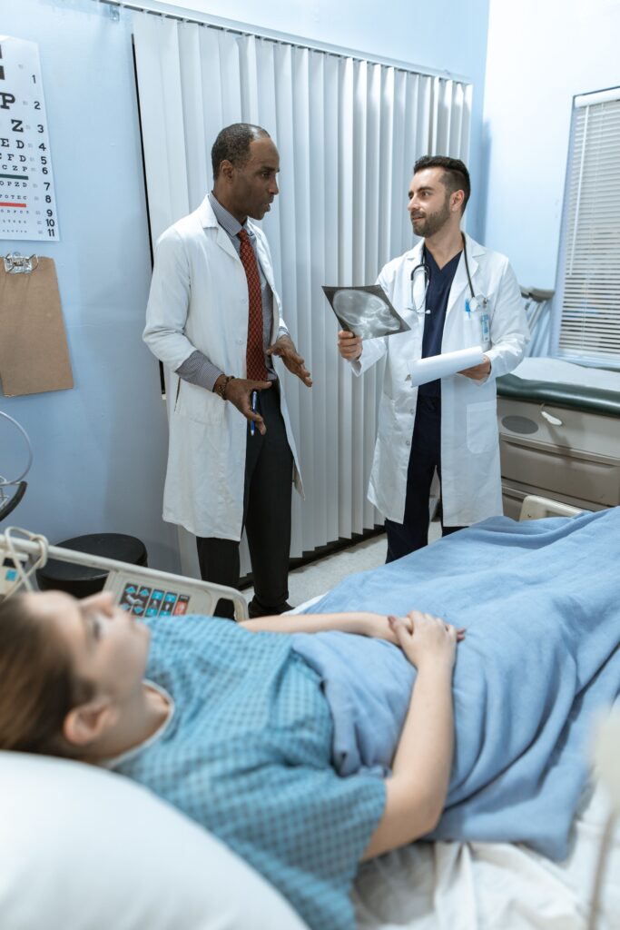 Two doctors discussing an image of a brain, likely one showing secondary hypoxic brain injury after initial injuries occurred. The patient is in the bed.