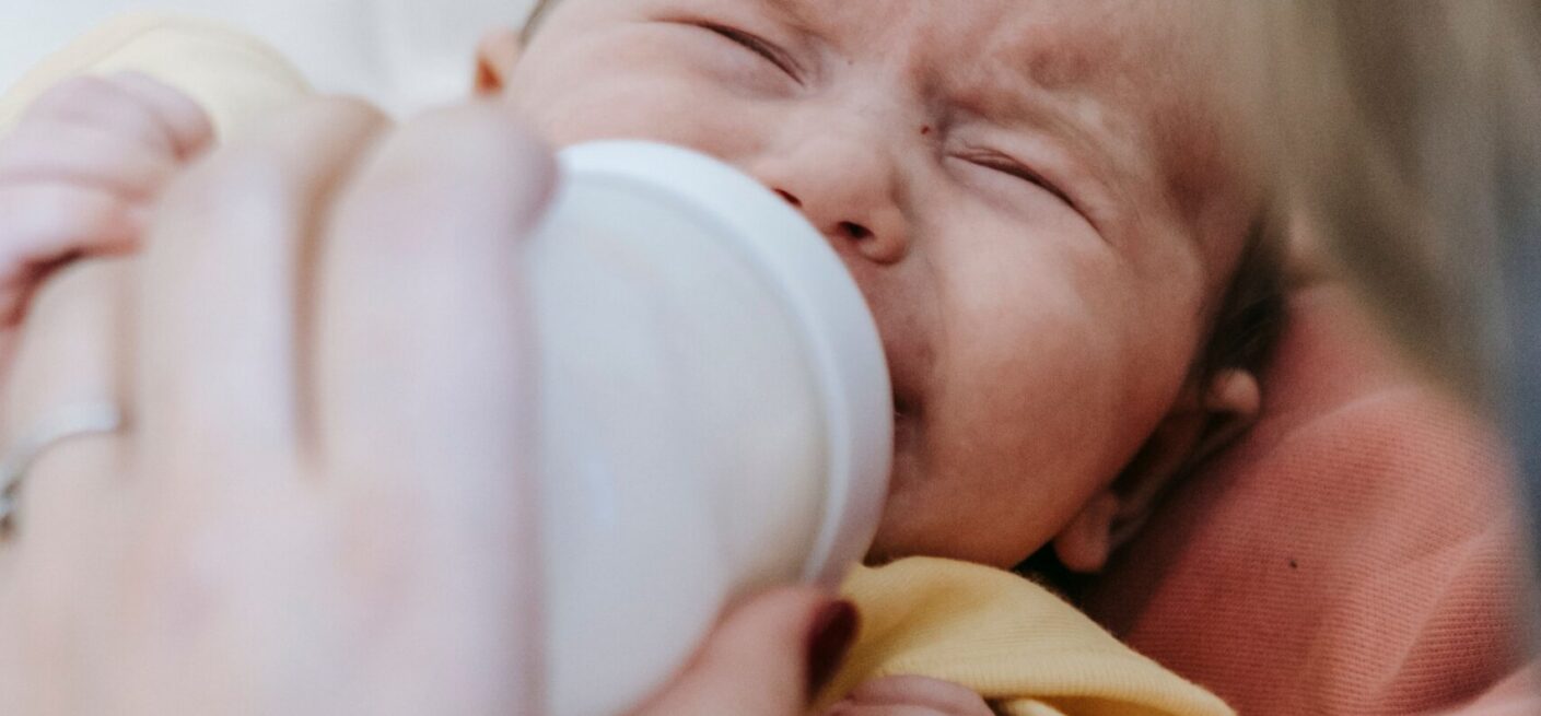 An infant struggling to drink milk, possibly caused by a condition known as galactosemia. The baby will need to be treated properly.